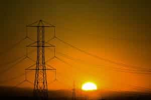 The sun is setting over a field of electricity pylons.