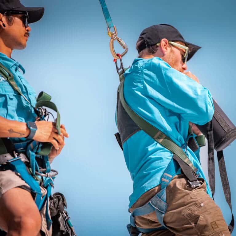 Two men wearing harnesses on top of a mountain.